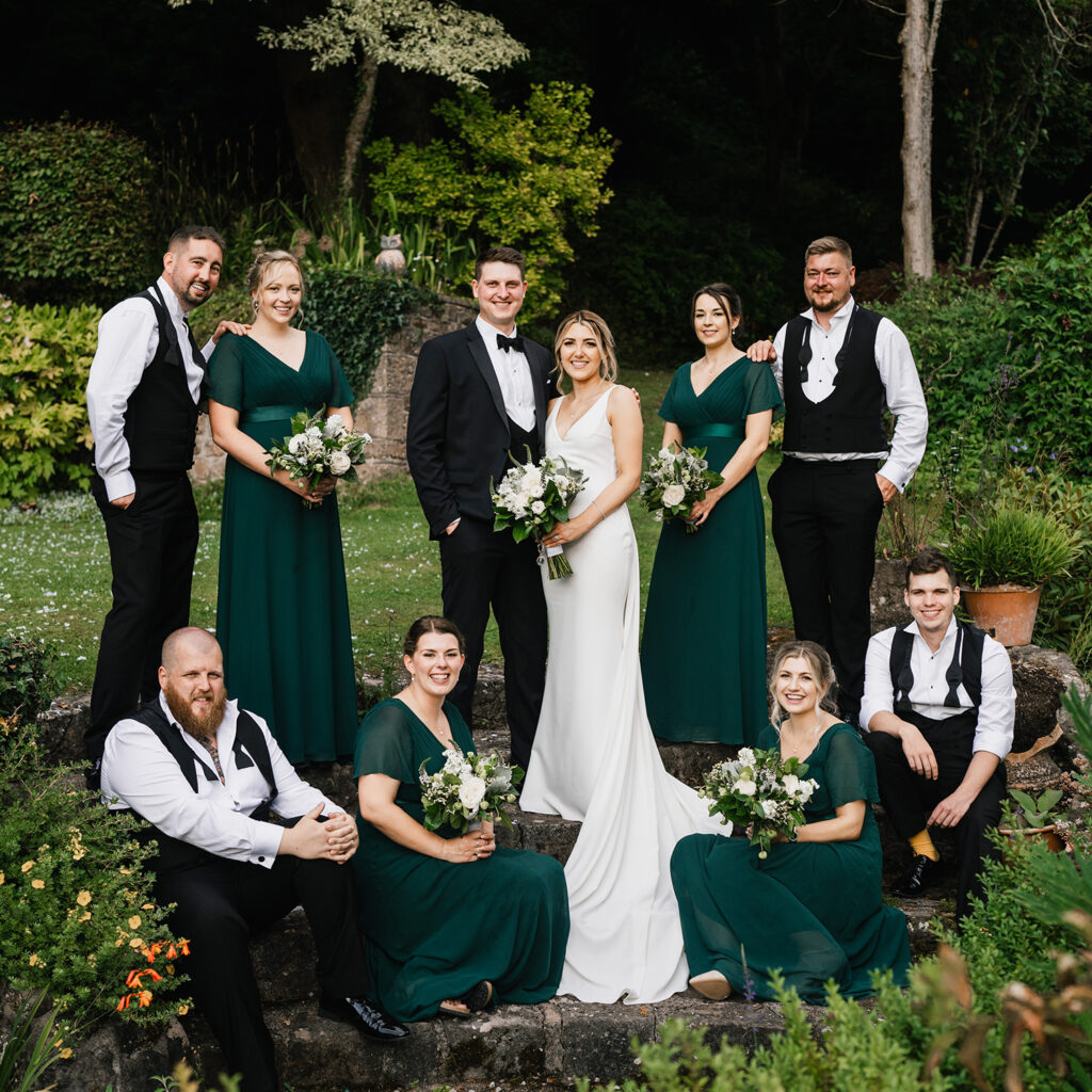 Wedding group on garden steps, bride and groom central, bridesmaids in green, groomsmen in suits.